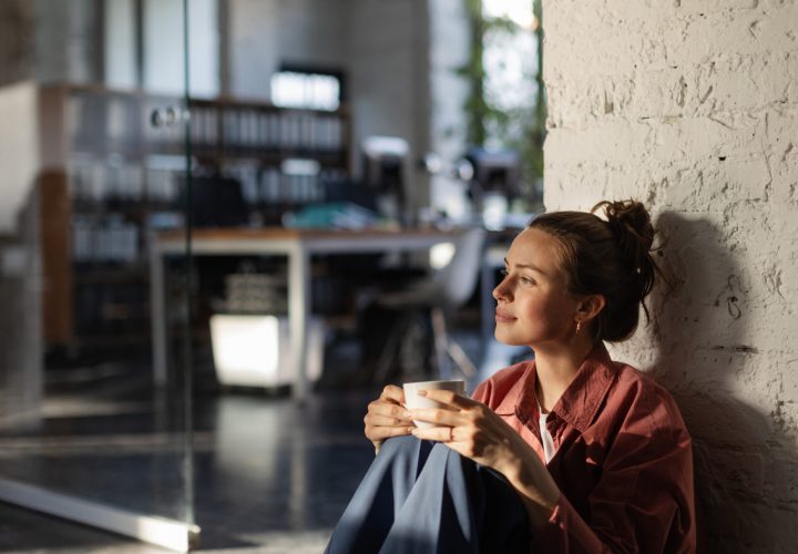 Happy female business owner in her own office drinking coffee and watching sunset.
